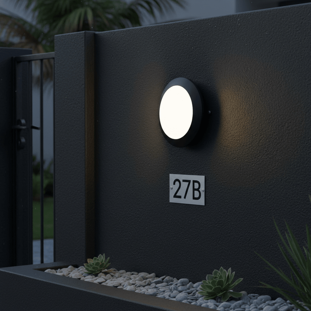 Outdoor wall light mounted on a dark wall, illuminating a pathway with decorative stones and a house number.