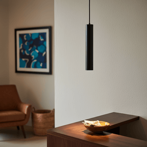 Slim black GU10 pendant light hanging above a wooden surface with a bowl and papers, modern decor.