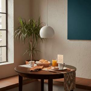 White metal dome pendant light hanging above a dining table with breakfast items and a plant.