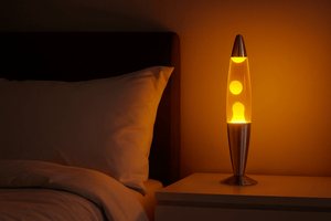 Red and yellow lava lamp on a bedside table, illuminating a bedroom with a warm glow.