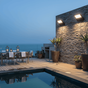 Coastal floodlight illuminating a stylish outdoor dining area by a pool at dusk.