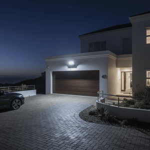 Coastal floodlight illuminating a driveway at night, mounted on a wall beside a garage.