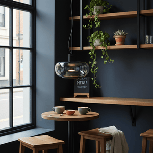 Modern green-tinted glass pendant light hanging above a wooden table with coffee cups and a small plant.