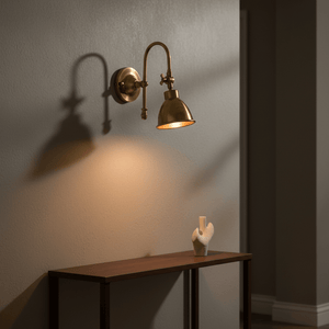 Antique brass wall lamp with a curved neck, casting warm light over a wooden table with a decorative sculpture.