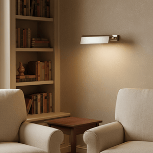 Goya Wall Lamp in antique silver illuminating a cozy reading nook with bookshelves and armchairs.