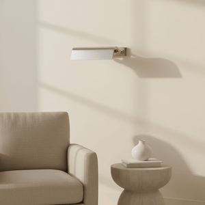 Antique silver wall lamp mounted above a cozy beige armchair, casting soft shadows on the wall.