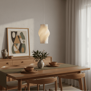 A modern white pendant light hangs above a wooden dining table set with bowls and a vase, complemented by a wall art piece.