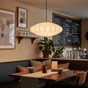 Silk Pendant Light hanging above a cozy dining table with coffee cups and a plant in a modern cafe setting.