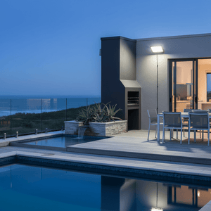 Coastal floodlight illuminating a modern patio area with a pool and ocean view at dusk.
