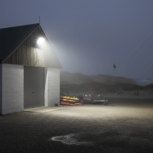 Coastal floodlight illuminating a storage shed at dusk, enhancing visibility in a foggy outdoor setting.