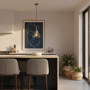Gold pendant light hanging above a modern kitchen island with two chairs and a plant in the background.