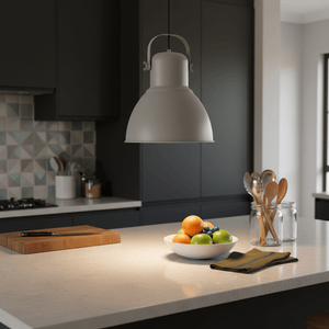 Grey steel pendant light hanging above a kitchen island with a bowl of fruit and utensils in the background.