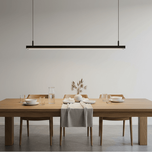Slim linear LED pendant light suspended above a wooden dining table set with plates and glasses.