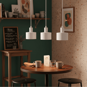 Three white metal pendant lights hang above a wooden table set with cups and a menu.