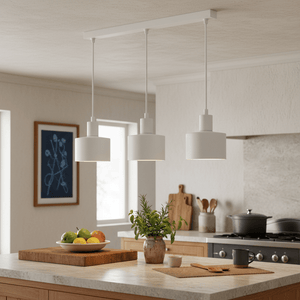 Three white metal pendant lights hang over a kitchen island with a bowl of fruit and a potted plant.