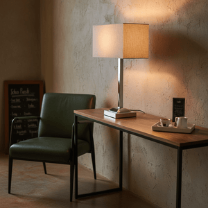 Polished chrome table lamp with champagne fabric shade on a wooden console table beside a green chair.