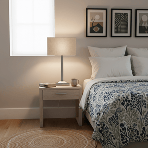 Polished chrome table lamp with champagne fabric shade on a bedside table, warm light illuminating the space.