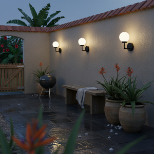 Three black Pearl LED wall lights with opal glass globes glow on a beige patio wall above a bench and potted plants at dusk