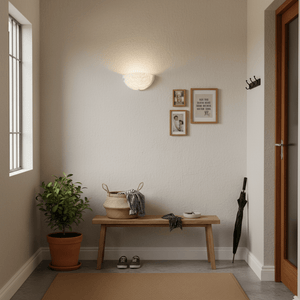 White glass indoor wall light illuminating a cozy entryway with a bench, plant, and framed photos.