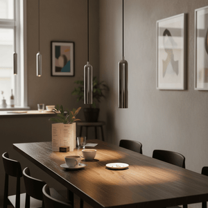 Sleek chrome pendant lights hanging over a wooden dining table, illuminating coffee cups and a dessert plate.