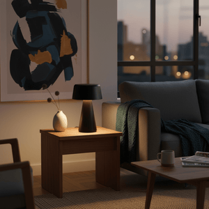 A modern black rechargeable table lamp on a wooden side table, casting a warm glow in a cozy living room setting.