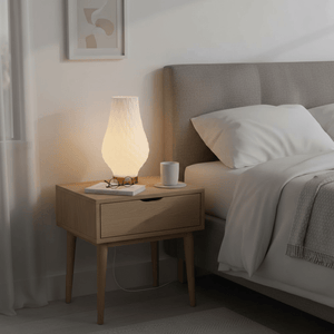 A modern 3D-printed table lamp on a bedside table, illuminating a cozy bedroom scene.