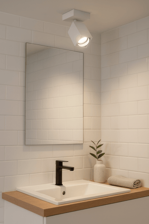 Square white spotlight mounted on ceiling above a modern bathroom sink with a mirror and plant.