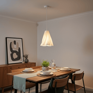 A white 3D printed pendant light hangs above a dining table set with plates and a vase of greenery.