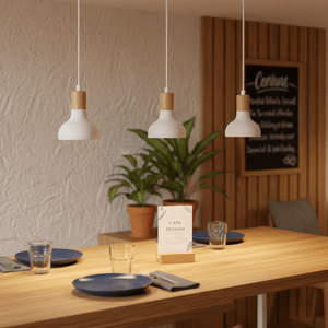 Three white pendant lights with wood accents hang above a wooden dining table set with plates and glasses.