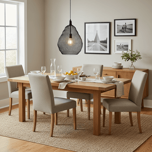 Black wire mesh pendant light hanging above a wooden dining table set with dishes and glasses.
