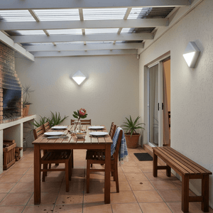 Outdoor setting featuring a wooden dining table with plates, illuminated by a diamond-shaped LED bulkhead light on the wall.