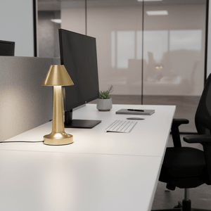 Gold rechargeable desk lamp on a modern office desk beside a computer and keyboard.