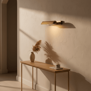Antique brass wall lamp illuminating a beige wall above a wooden console table with a vase and decor.