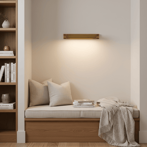 Goya Wall Lamp in antique brass illuminating a cozy reading nook with cushions and books.