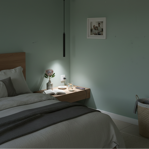 A slim black LED pendant light hangs above a bedside table with a flower vase, book, and glass.