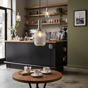 Athina Clear Cut Glass Pendant light hanging above a wooden table with coffee cups in a cozy café setting.