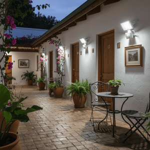 Outdoor corridor illuminated by motion sensor floodlights, featuring potted plants and a small table.