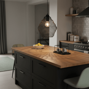 Phantom Black 340 wire mesh pendant light hanging over a kitchen island with a wooden countertop and decorative items.