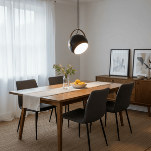 Black leather strap pendant light hanging over a wooden dining table with a vase and fruit bowl.