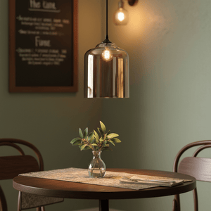 Amber bell jar pendant light hanging above a wooden dining table with a small vase of greenery.