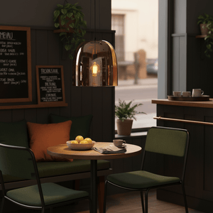 Amber dome pendant light hanging above a wooden table with green chairs, featuring a bowl of lemons and a coffee cup.