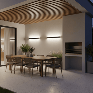 Modern outdoor dining area featuring a linear wall light illuminating a wooden table and barbecue.
