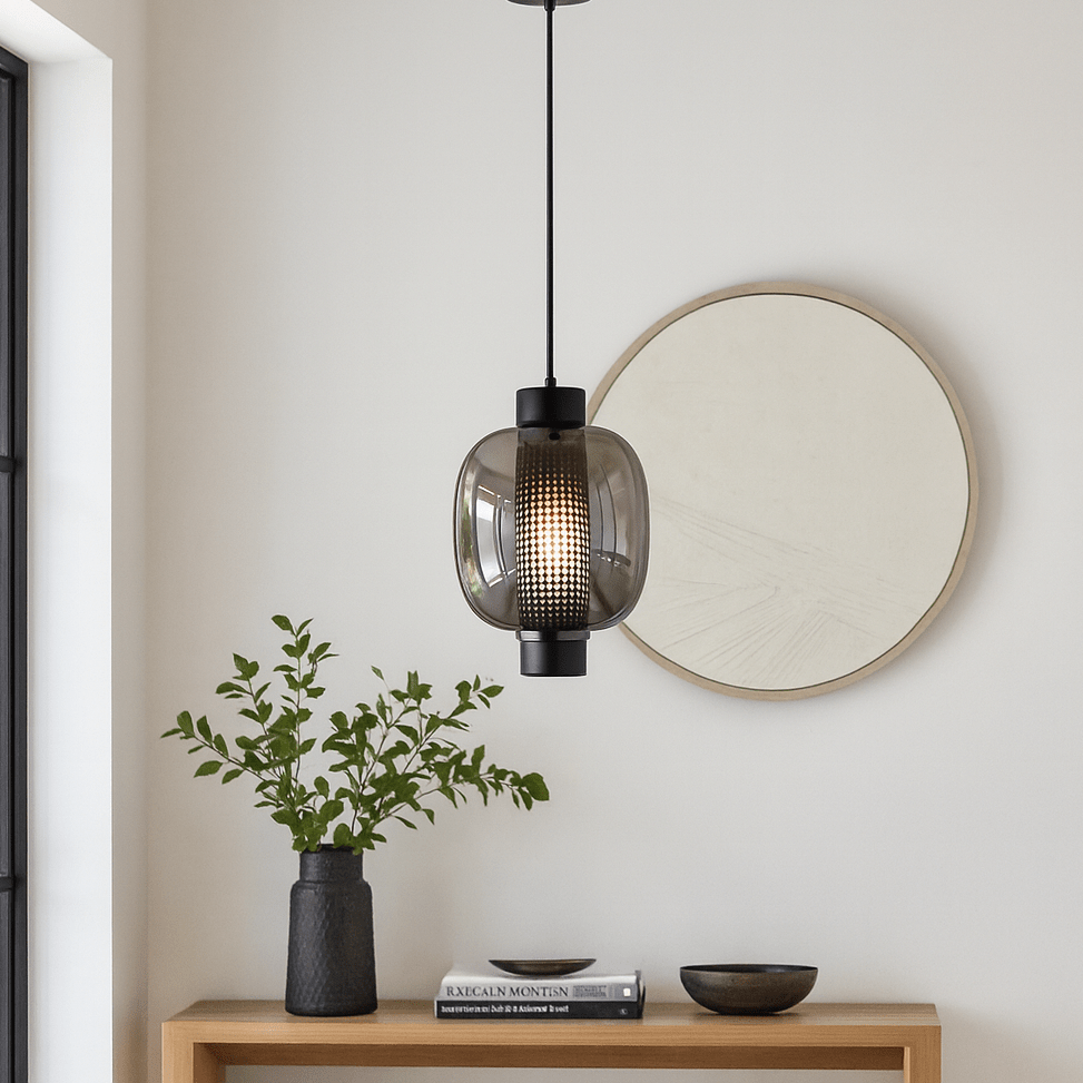 Modern black glass pendant light hanging above a wooden table with a plant and decorative items.