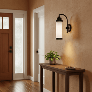 Kerala Wall Lamp in matt black mounted on a textured wall, illuminating a wooden console table with a plant.