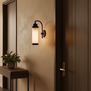 Kerala Wall Lamp in matt black mounted on a textured wall, illuminating a hallway with a plant and wooden console table.