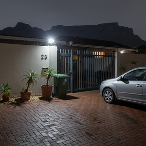 LED floodlight illuminating a driveway with potted plants and a parked car at night.