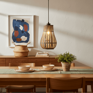 Metal and rattan pendant light hanging above a dining table set with bowls and a plant.