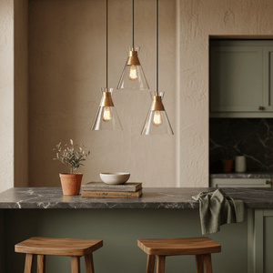 Three-light pendant featuring clear glass shades and gold accents, hanging above a kitchen island with wooden stools.