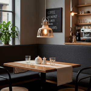 White metal pendant light with cognac glass shade hanging above a wooden table set with glassware and a teapot.