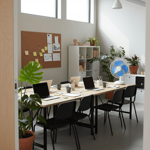 A modern office space featuring a desk fan on a table surrounded by laptops and plants.